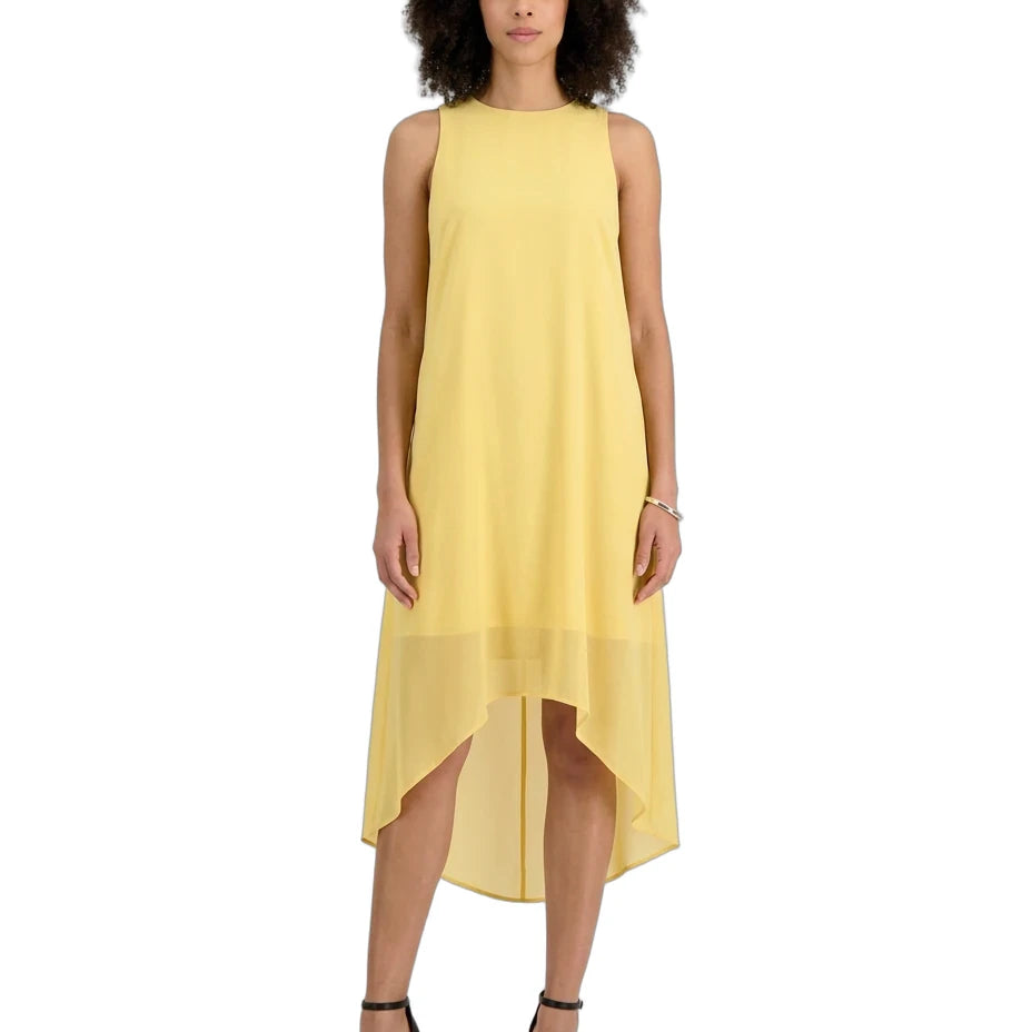 A woman modeling a sleeveless high-low midi dress in a soft pastel yellow, paired with black strappy high-heeled sandals against a plain white background.