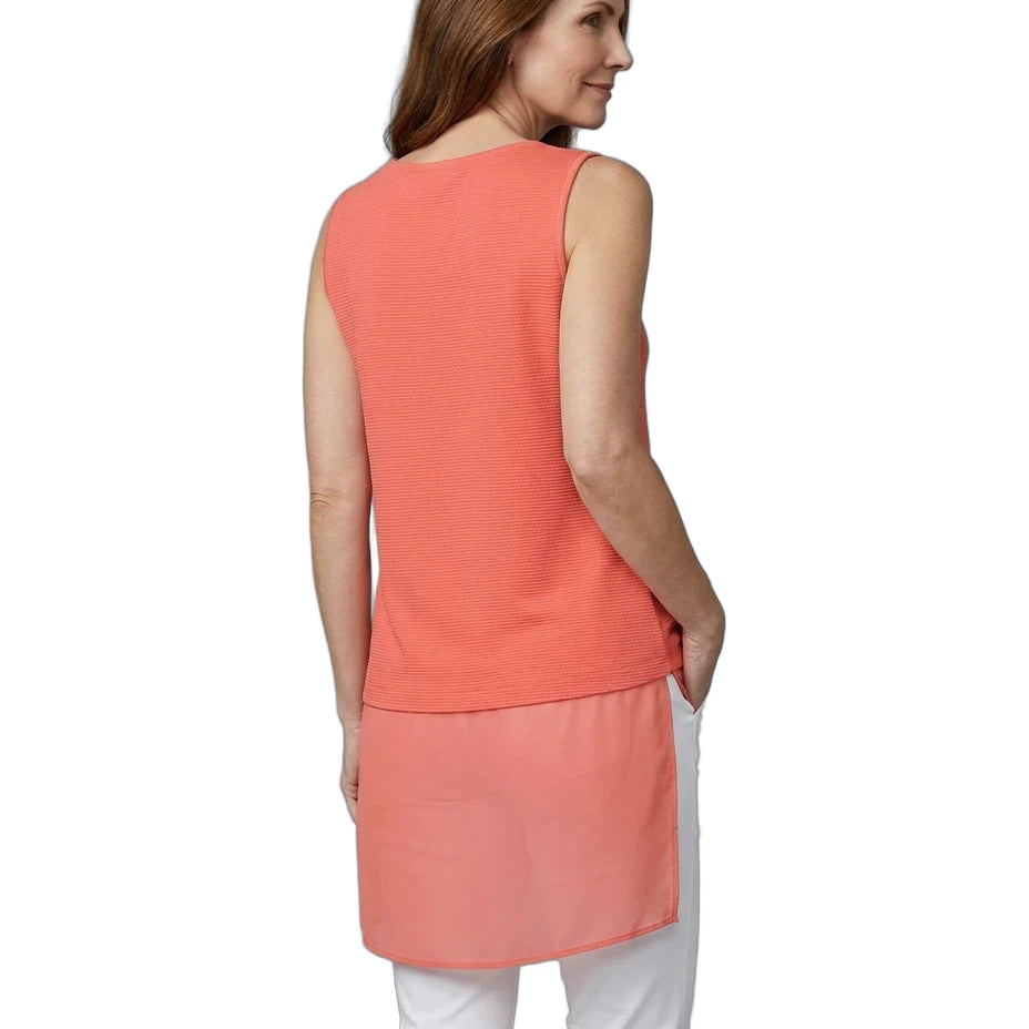 Woman wearing a coral sleeveless top and white pants on a white background