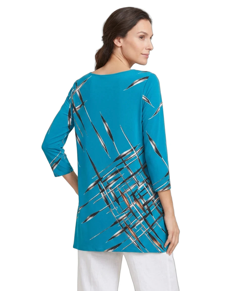 A woman shown from the back wearing a turquoise blue tunic top with a black, white, and gray brushstroke pattern, paired with white pants, against a plain white background.