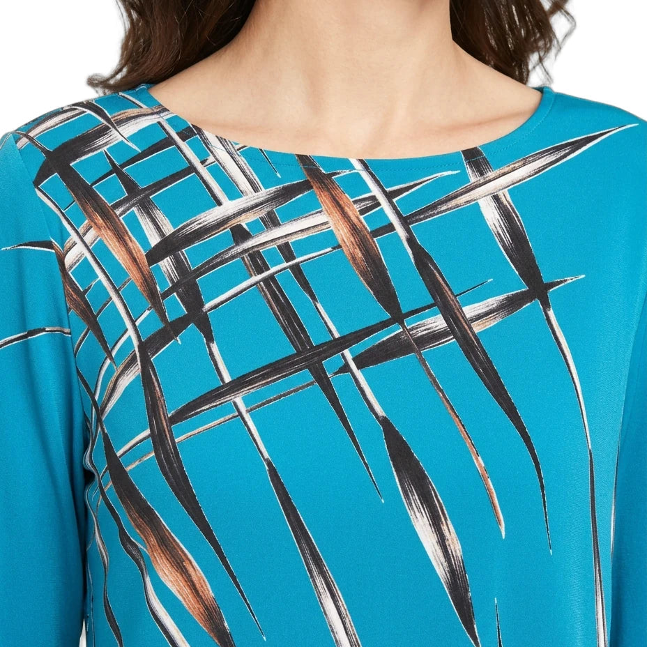A close-up of a model wearing a bright turquoise blue top with a black, white, and brown abstract leaf-like pattern across the chest.