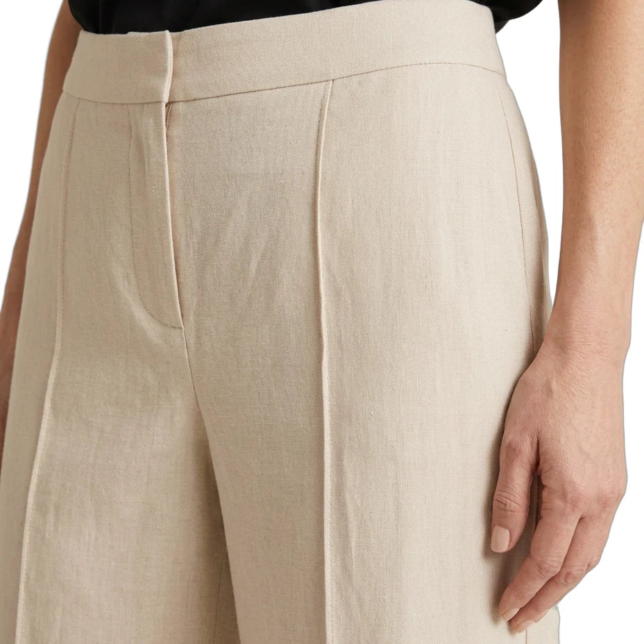 Close-up of a person wearing high-waisted, wide-leg trousers in a light beige linen-like fabric, paired with a black top against a plain white background.