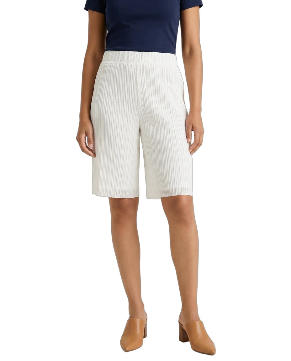 A model wearing white pleated knee-length shorts, a navy blue top, and tan mule heels, shown from the waist down against a plain white background.