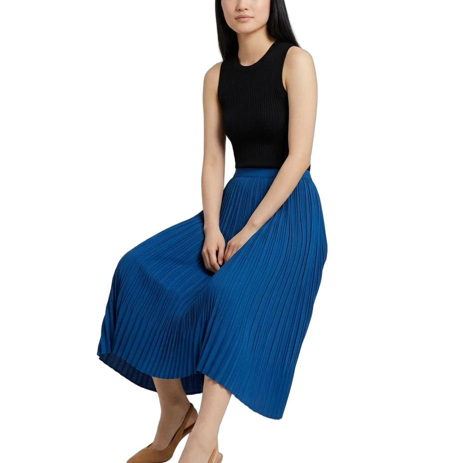 A woman wearing a sleeveless black top and a pleated royal blue midi skirt, paired with tan pointed-toe heels, posed against a solid white background.