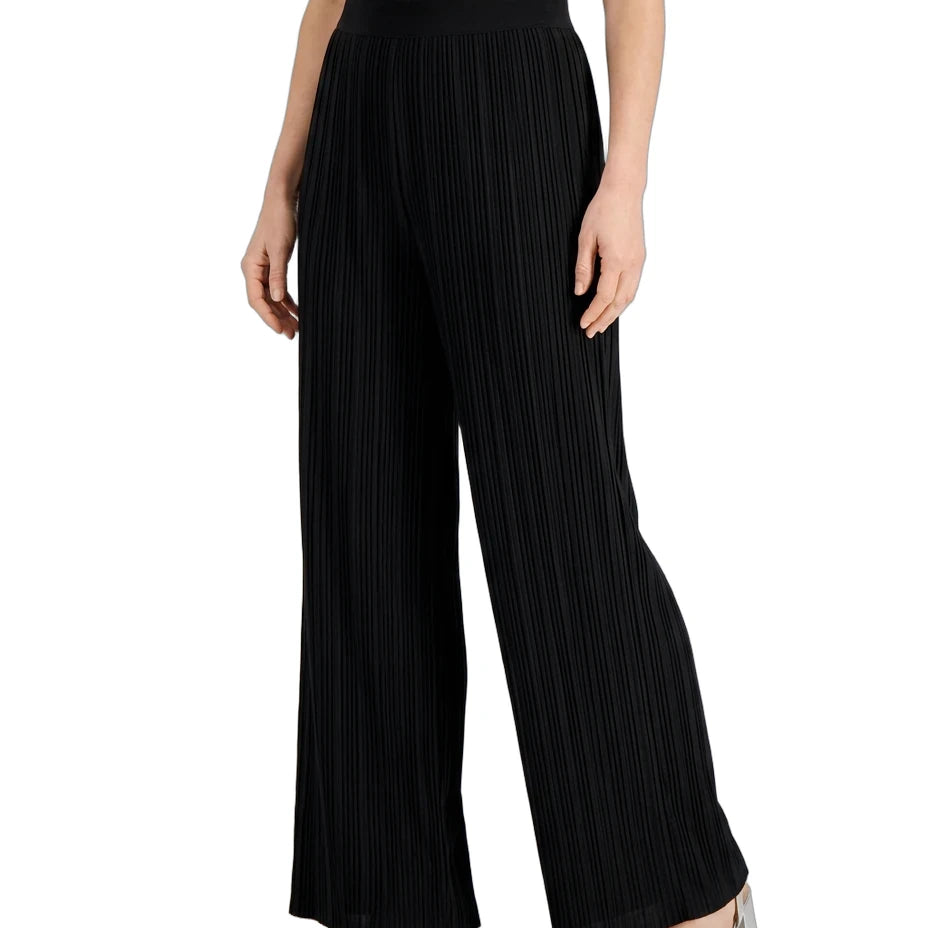 Black wide-leg pleated trousers worn by a model, paired with a cream top and metallic silver block-heel sandals, shown against a plain white background.
