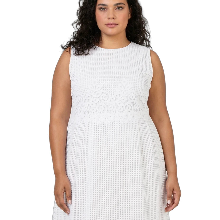 A woman modeling a sleeveless white dress with a textured eyelet pattern and a decorative embroidered band at the waist, shot against a plain white background.