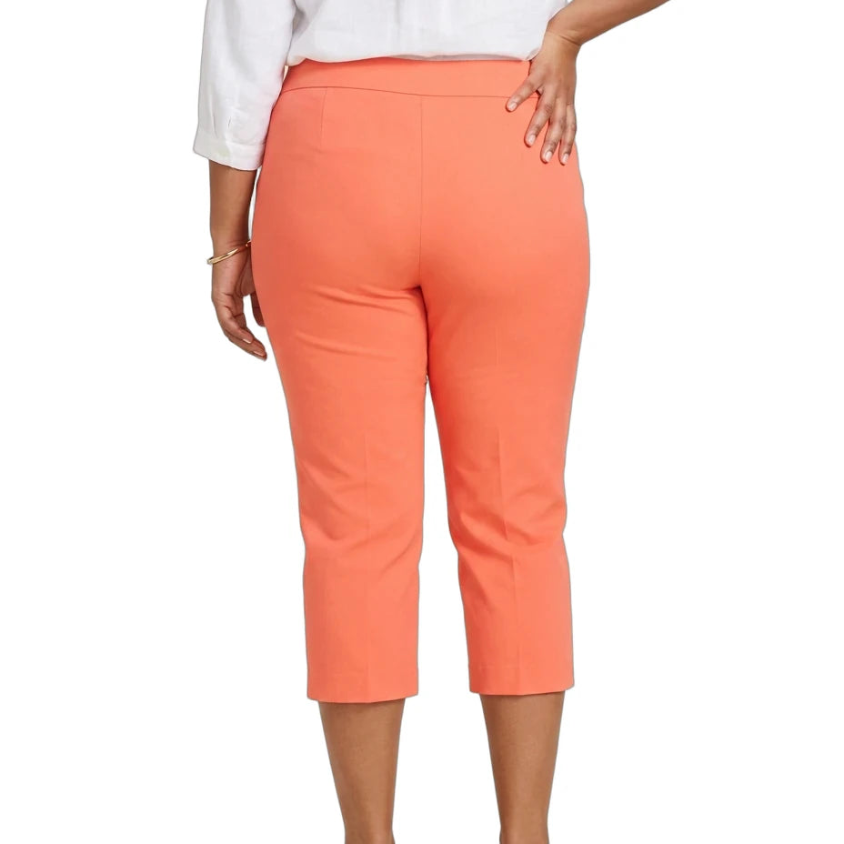 A woman shown from the back wearing bright coral-orange cropped capri pants, a white blouse, and tan flat sandals against a plain white studio background.