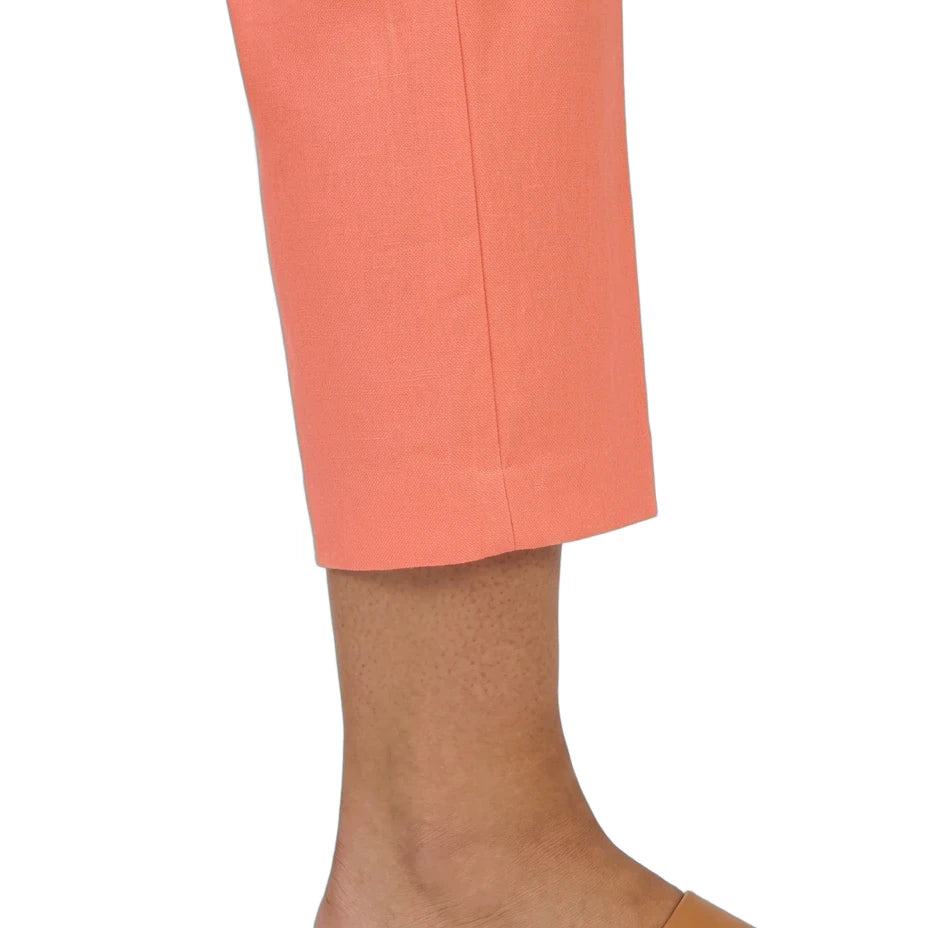 A close-up of a person's lower leg and foot wearing cropped peach-pink trousers and tan slide sandals against a plain white background.
