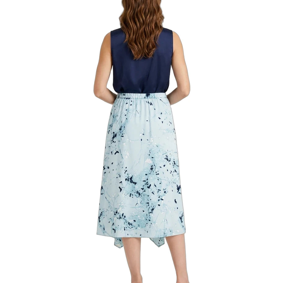 A woman viewed from the back wearing a sleeveless dress with a navy blue bodice and a light blue watercolor-style printed skirt, paired with tan block-heel sandals on a white background.