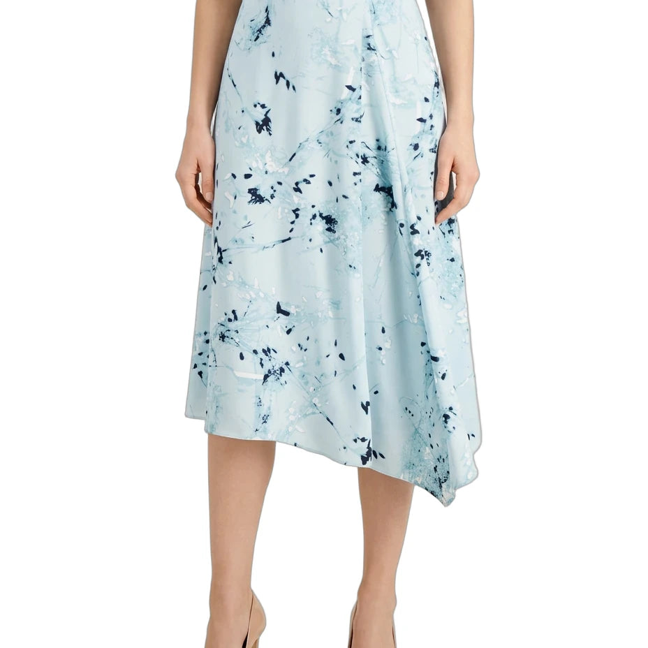 A model wearing a light blue midi skirt with a dark blue abstract floral print, paired with a navy top and beige high heels, shown against a plain white background.