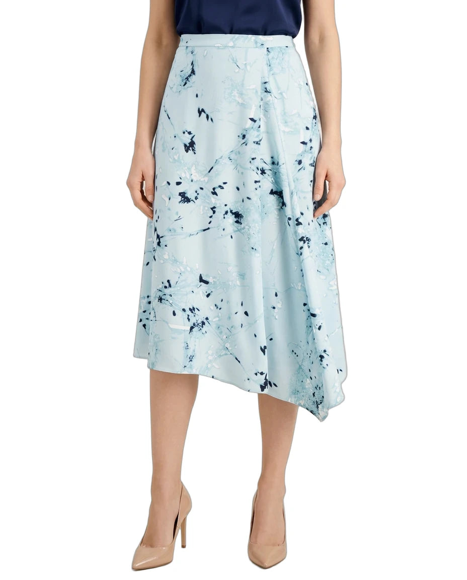 A model wearing a light blue midi skirt with a dark blue abstract floral print, paired with a navy top and beige high heels, shown against a plain white background.
