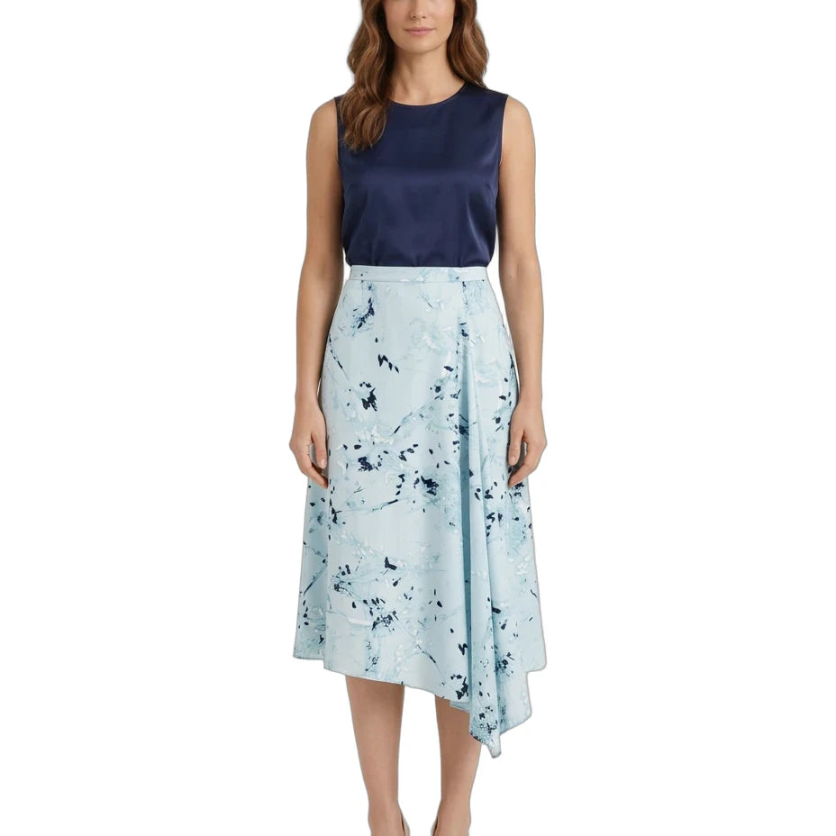 A woman modeling a sleeveless midi dress with a dark navy blue satin bodice and a light blue wrap-style skirt featuring a dark blue abstract floral print, set against a plain white background.