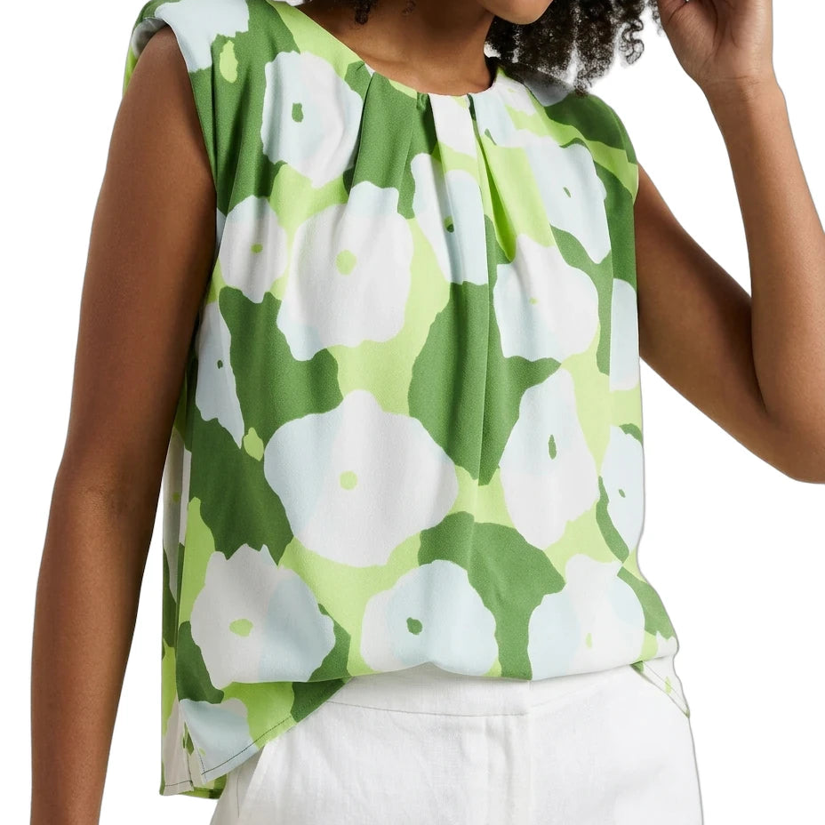Woman wearing a green floral sleeveless top with white pants on a plain background