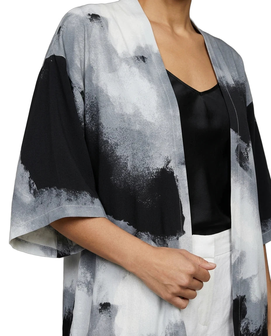 Person wearing a black and white abstract patterned kimono over a black top and white pants.