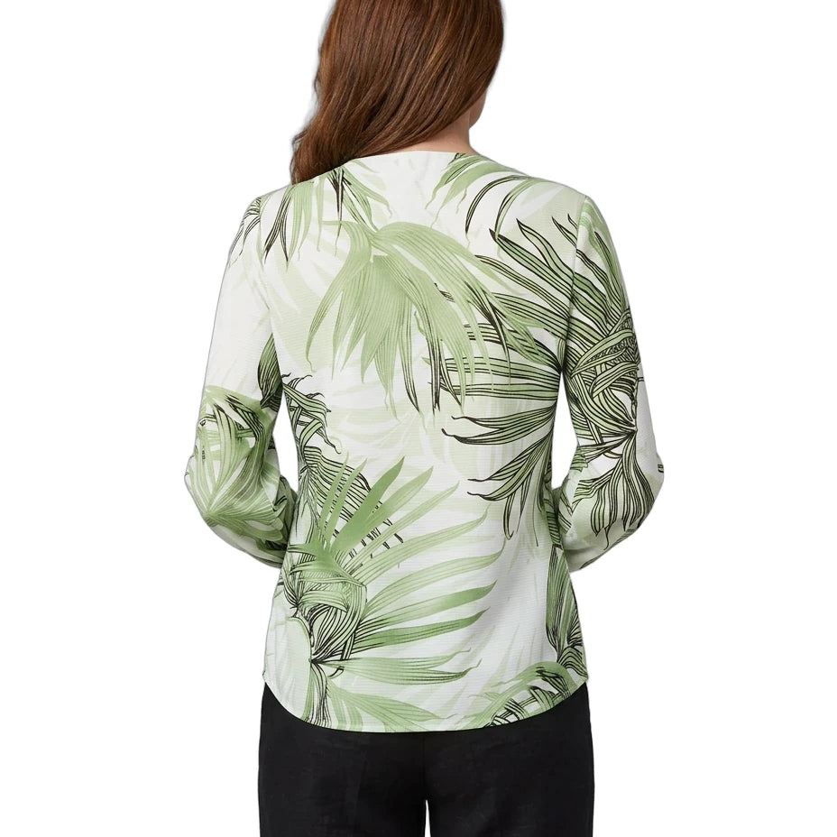 A woman viewed from the back wearing a long-sleeve blouse with a green palm leaf pattern on a white background, paired with black pants, against a plain white studio background.