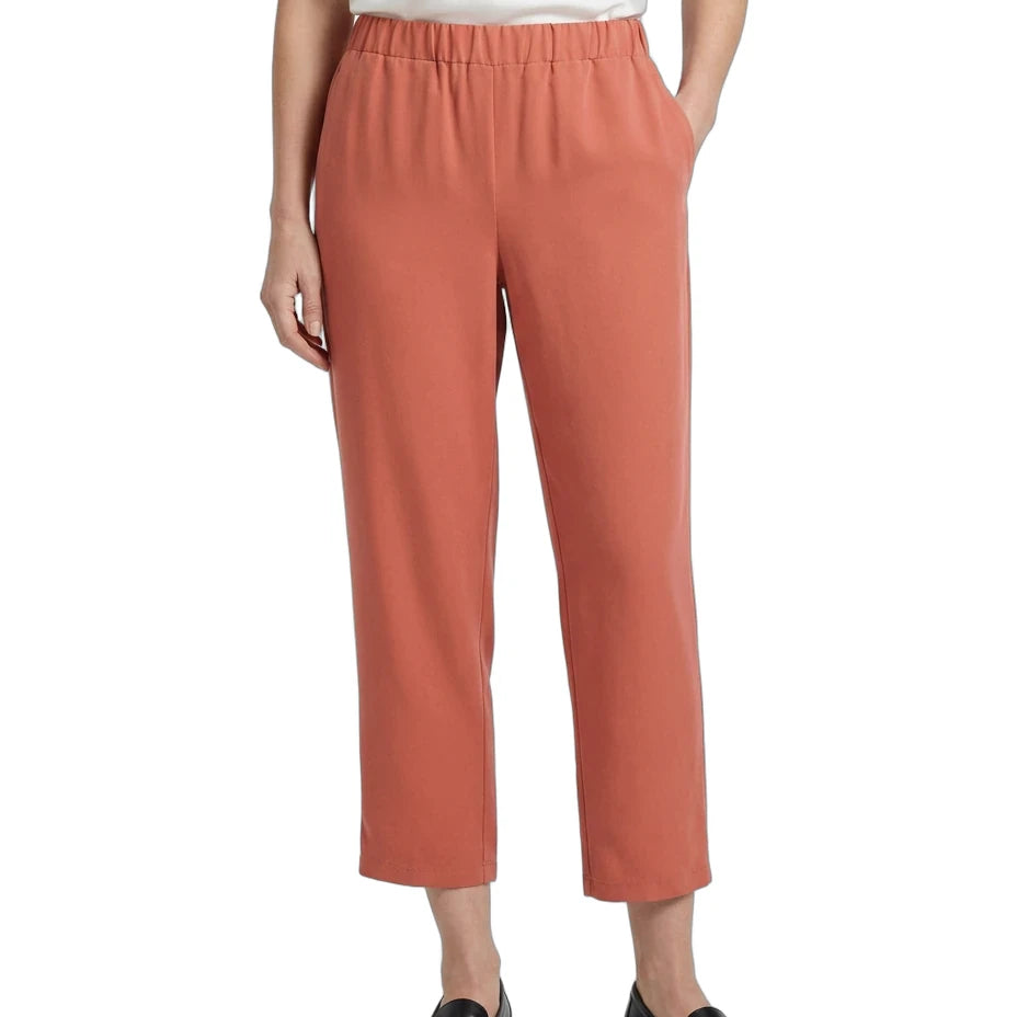 A model wearing a pair of cropped, wide-leg trousers in a muted terracotta or dusty rose color, paired with a white top and black loafers, shown against a plain white background.