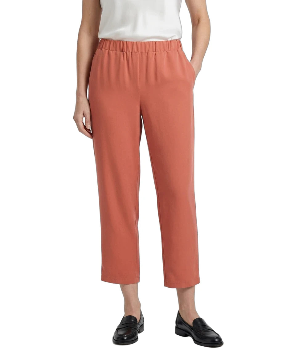 A model wearing a pair of cropped, wide-leg trousers in a muted terracotta or dusty rose color, paired with a white top and black loafers, shown against a plain white background.