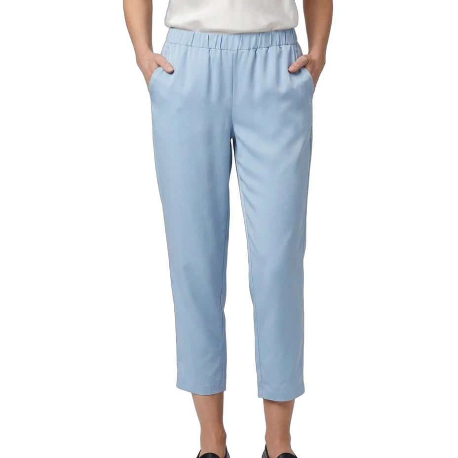 A model wearing light blue cropped trousers with an elastic waistband and side pockets, paired with a white top and black loafers, shown against a plain white background.