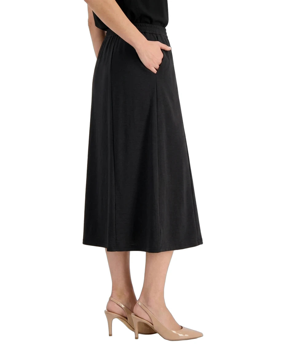 A model wearing a black midi skirt with side pockets, paired with beige slingback heels, shown from the waist down against a plain white background.
