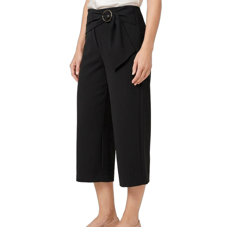 A model wearing black cropped wide-leg pants with a matching fabric tie belt and round metal buckle, styled with a white top and beige flats against a white background.