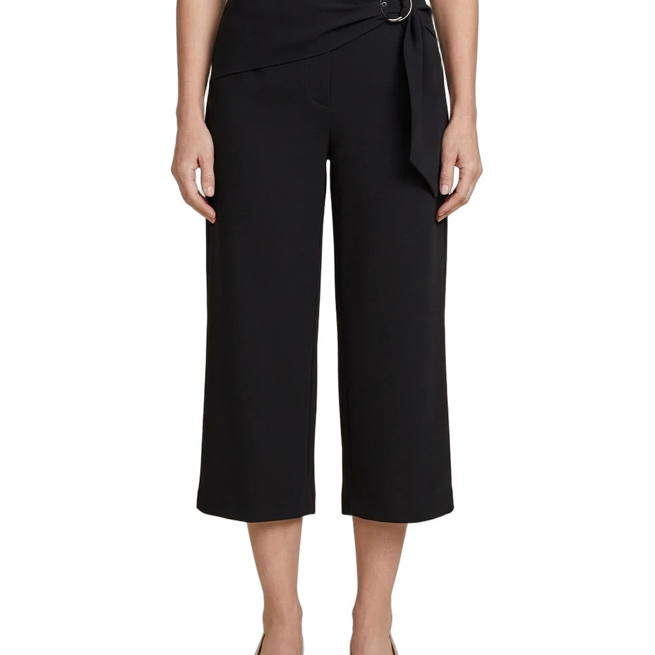 A model wearing black cropped wide-leg pants with a wrap-style waist and a silver-tone circular belt buckle, paired with a white top and beige heels against a plain white background.