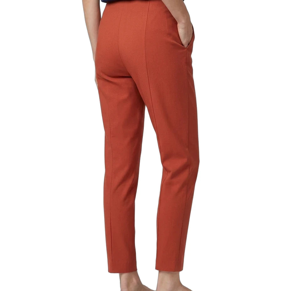 A person shown from the back wearing rust-orange cropped trousers, a navy top, and black flats against a plain white studio background.