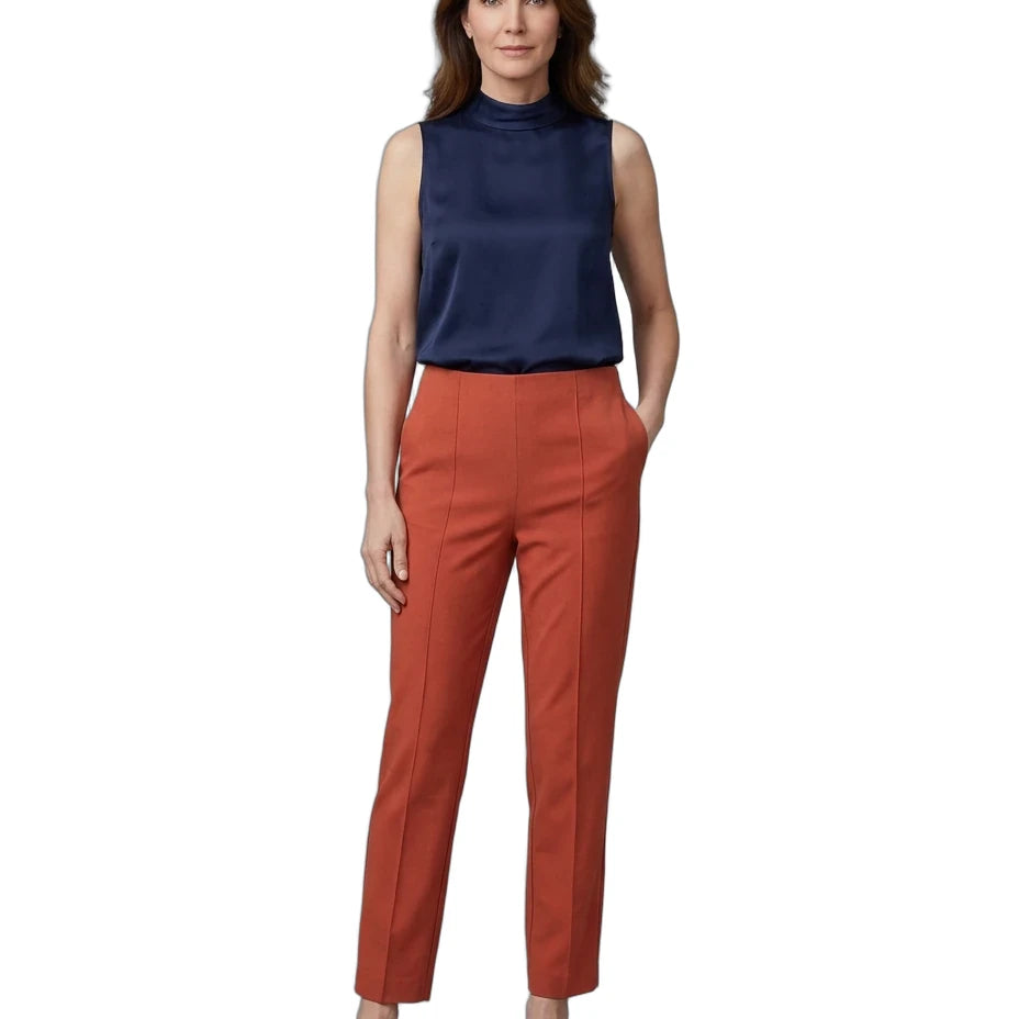 A woman modeling a sleeveless navy blue mock-neck top and rust-orange cropped trousers with black flats, shot against a plain white background.