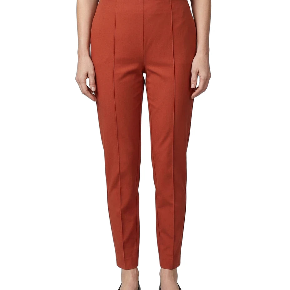 A model wearing a pair of rust-orange cropped trousers with front crease details, paired with a navy top and black flats, shown against a plain white background.