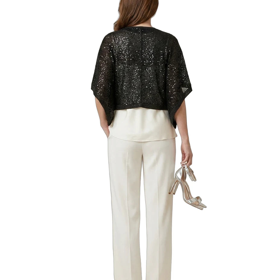 Woman wearing a black sequin top and white pants on a white background