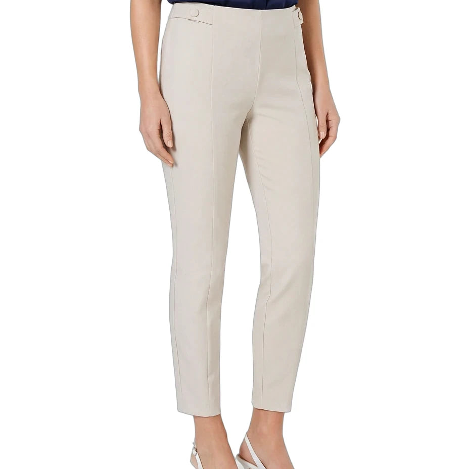 A model wearing a pair of slim-fit, ankle-length cropped trousers in a light beige color, styled with a navy blue top and white pointed-toe heels against a plain white background.