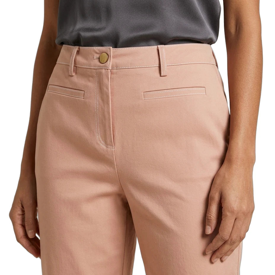 A close-up of a model wearing dusty pink tailored trousers with belt loops, a button closure, and front welt pockets, paired with a dark gray top against a white background.
