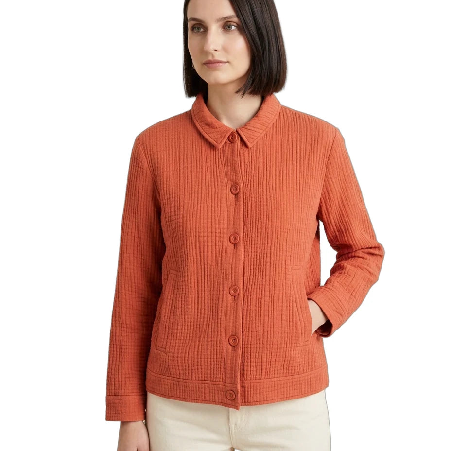 A woman wearing a textured, ribbed orange cardigan with a button-down front and collar, paired with cream pants, against a plain white background.