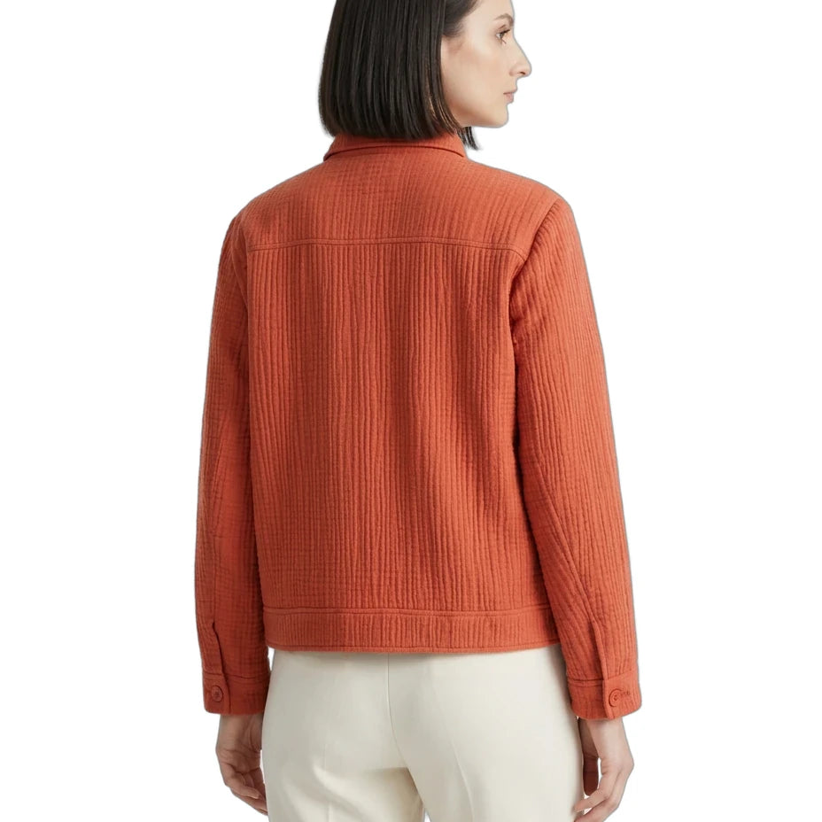 A woman shown from the back wearing a textured rust-orange quilted jacket and cream-colored trousers, photographed against a solid white background.