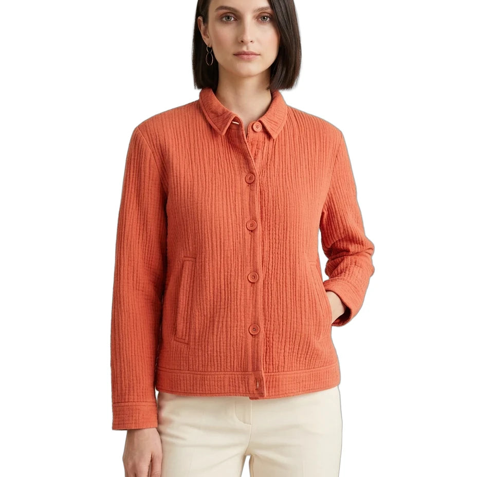 A woman modeling a textured, ribbed orange button-up cardigan with a collar and front pockets, paired with cream pants, against a plain white background.
