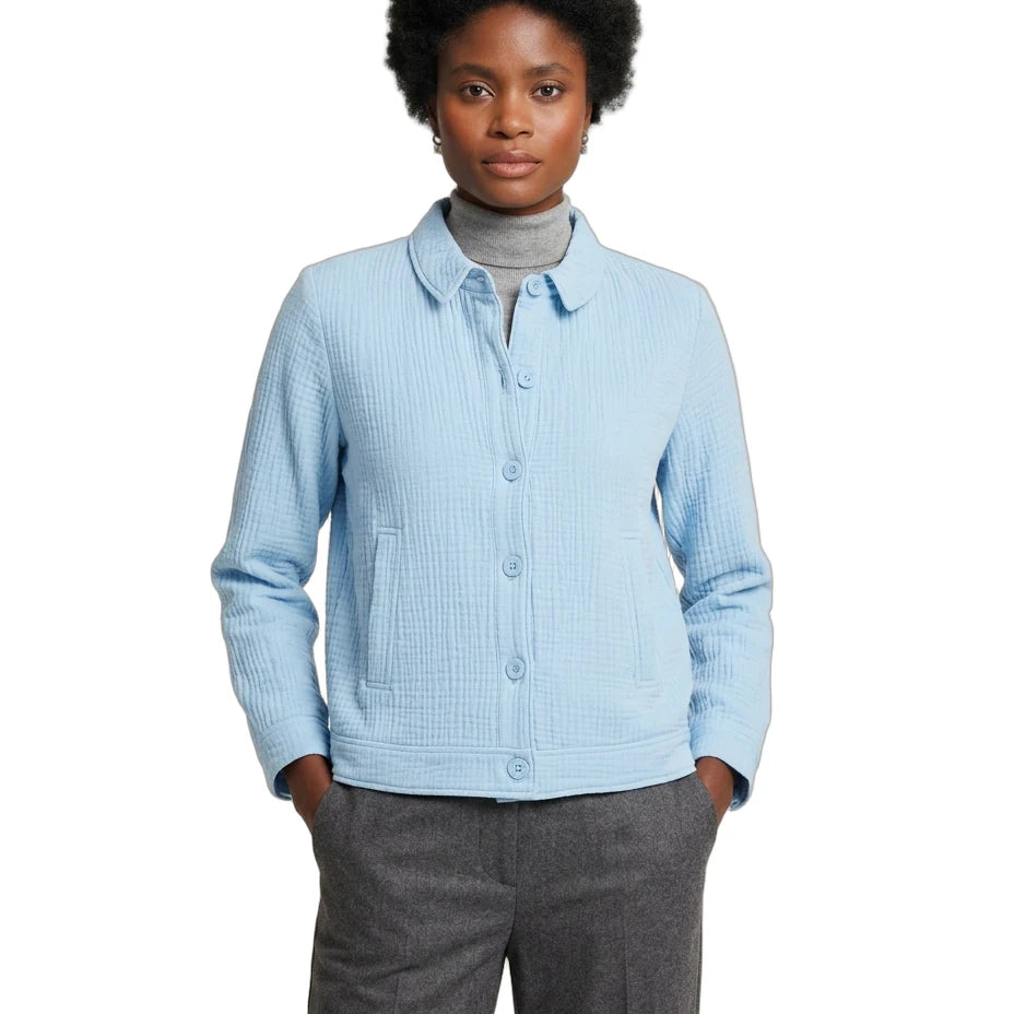 A woman modeling a light blue textured button-up cardigan over a gray turtleneck, paired with gray trousers, against a plain white background.