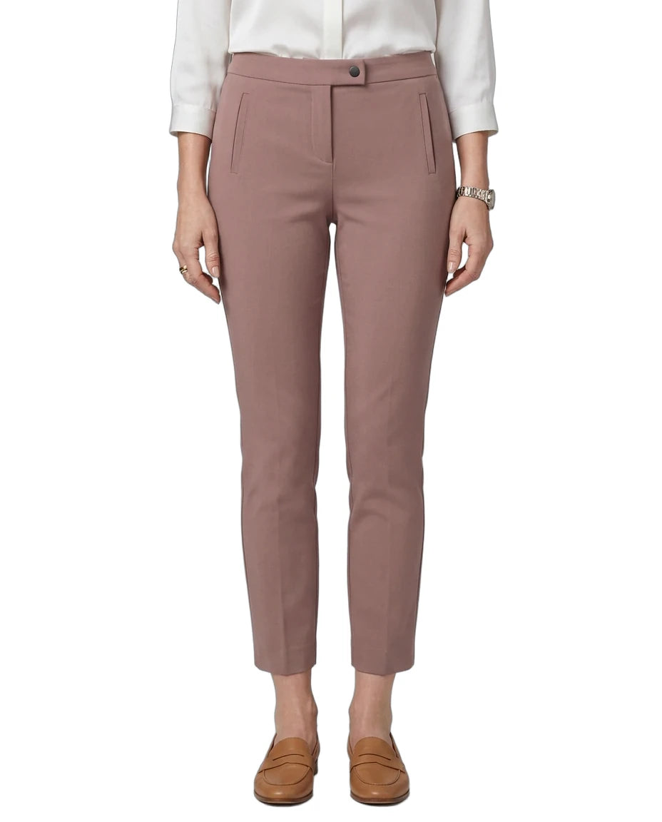 A model wearing slim-fit, ankle-length trousers in a dusty rose pink color, paired with a white long-sleeve blouse and brown leather loafers, shown against a plain white background.