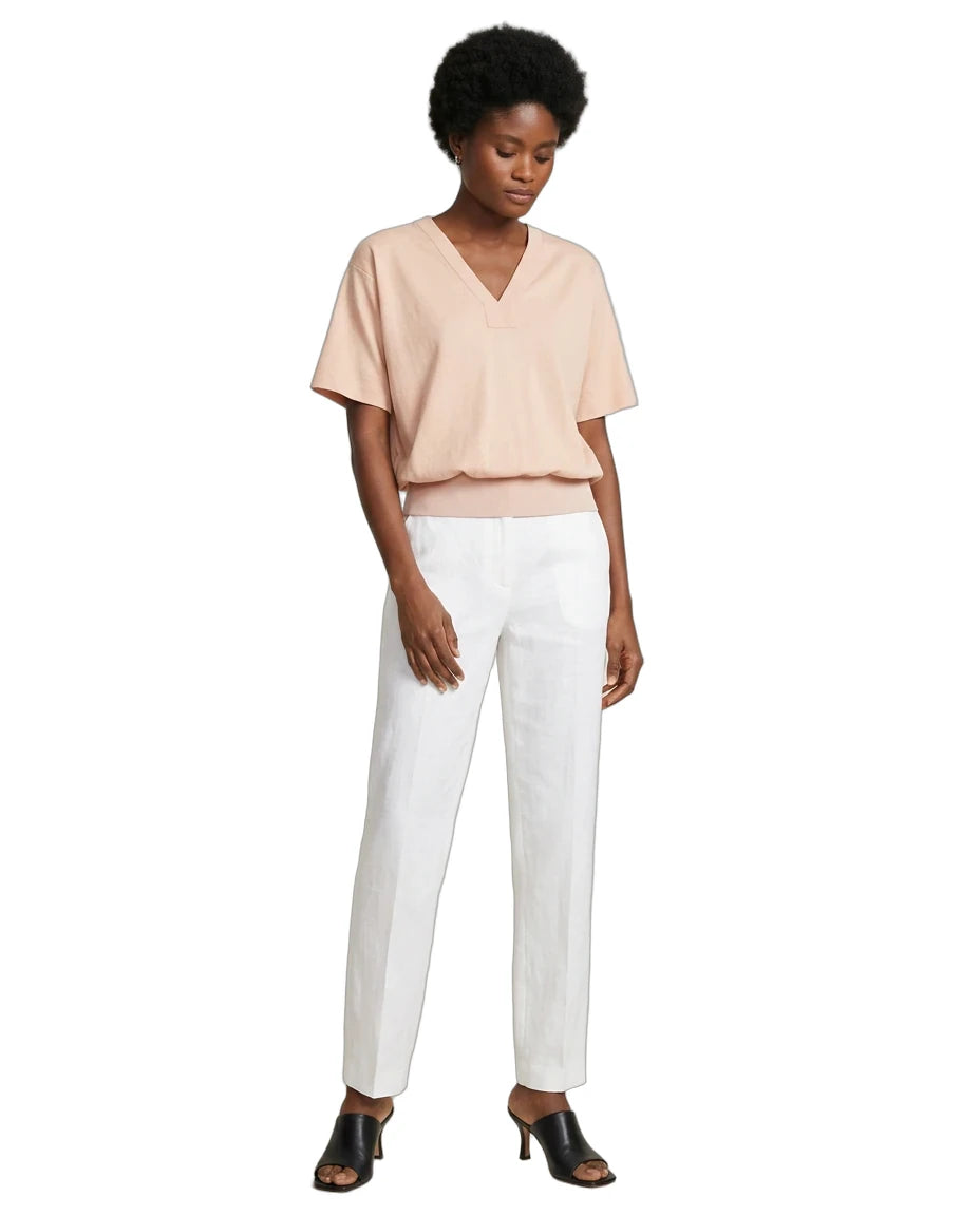 A model wearing a light peach V-neck short-sleeve top and white straight-leg trousers, paired with black heeled mule sandals, against a plain white background.