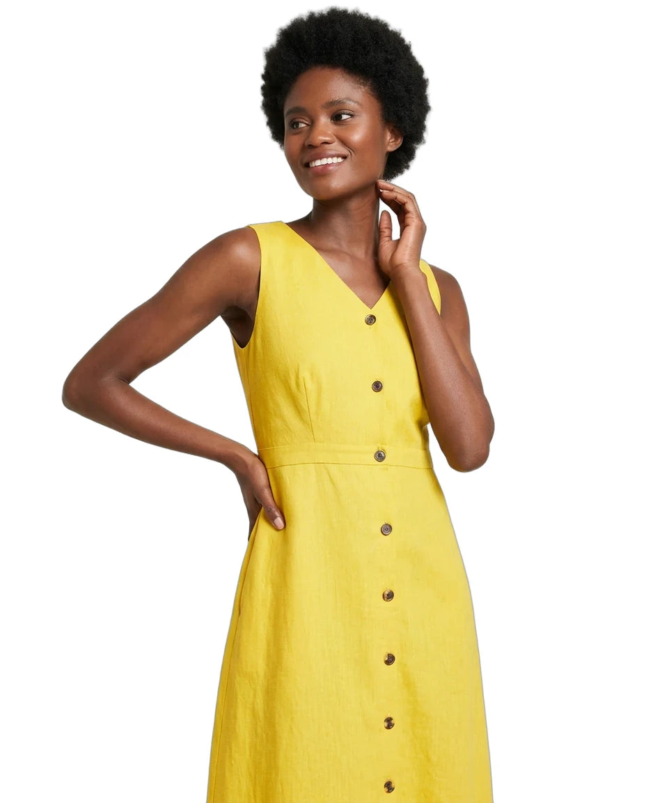 A woman modeling a sleeveless yellow linen dress with a button-down front, photographed against a solid white background.