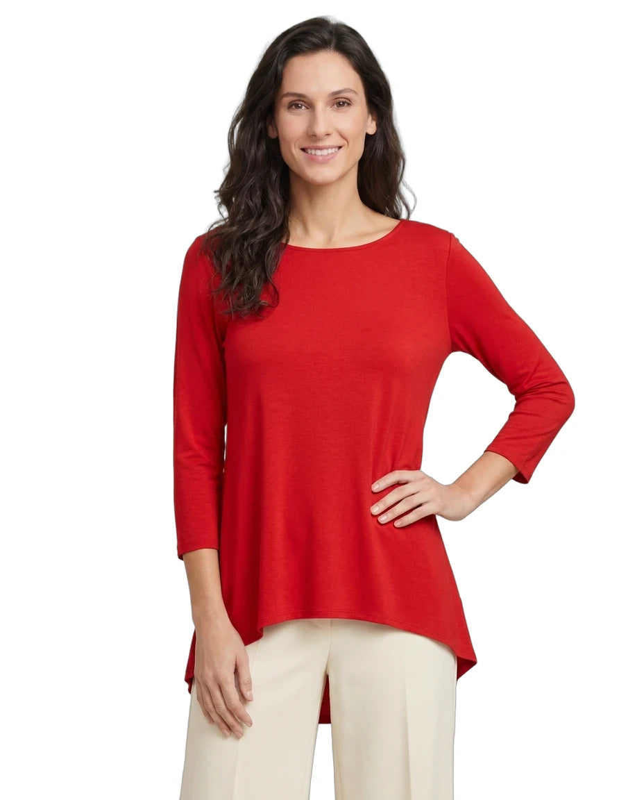 A woman modeling a bright red three-quarter sleeve top with a high-low hem, paired with cream pants, against a plain white background.