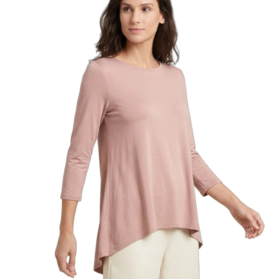 A woman modeling a dusty pink three-quarter sleeve top with an asymmetrical handkerchief hem, paired with cream pants, against a plain white background.