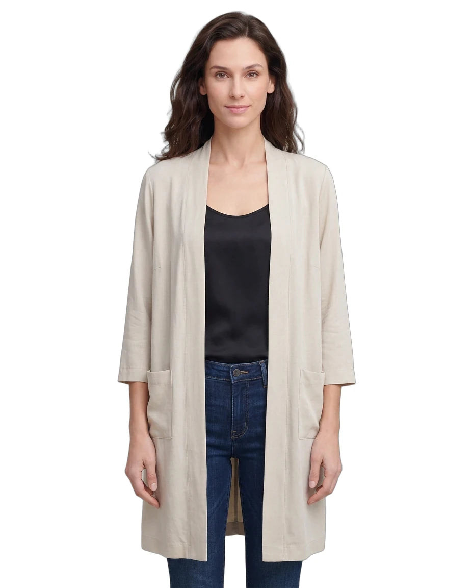 Woman wearing a beige cardigan over a black top and blue jeans on a white background