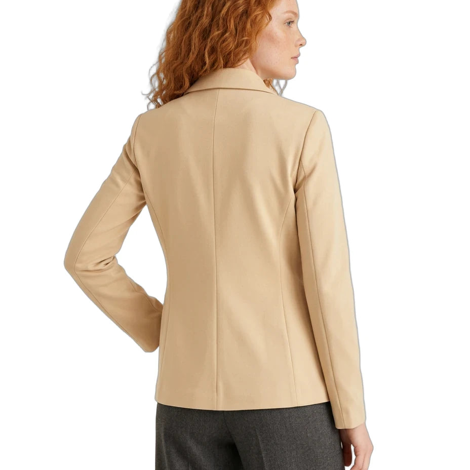 A woman with red curly hair is shown from the back wearing a beige tailored blazer and dark gray trousers against a plain white background.