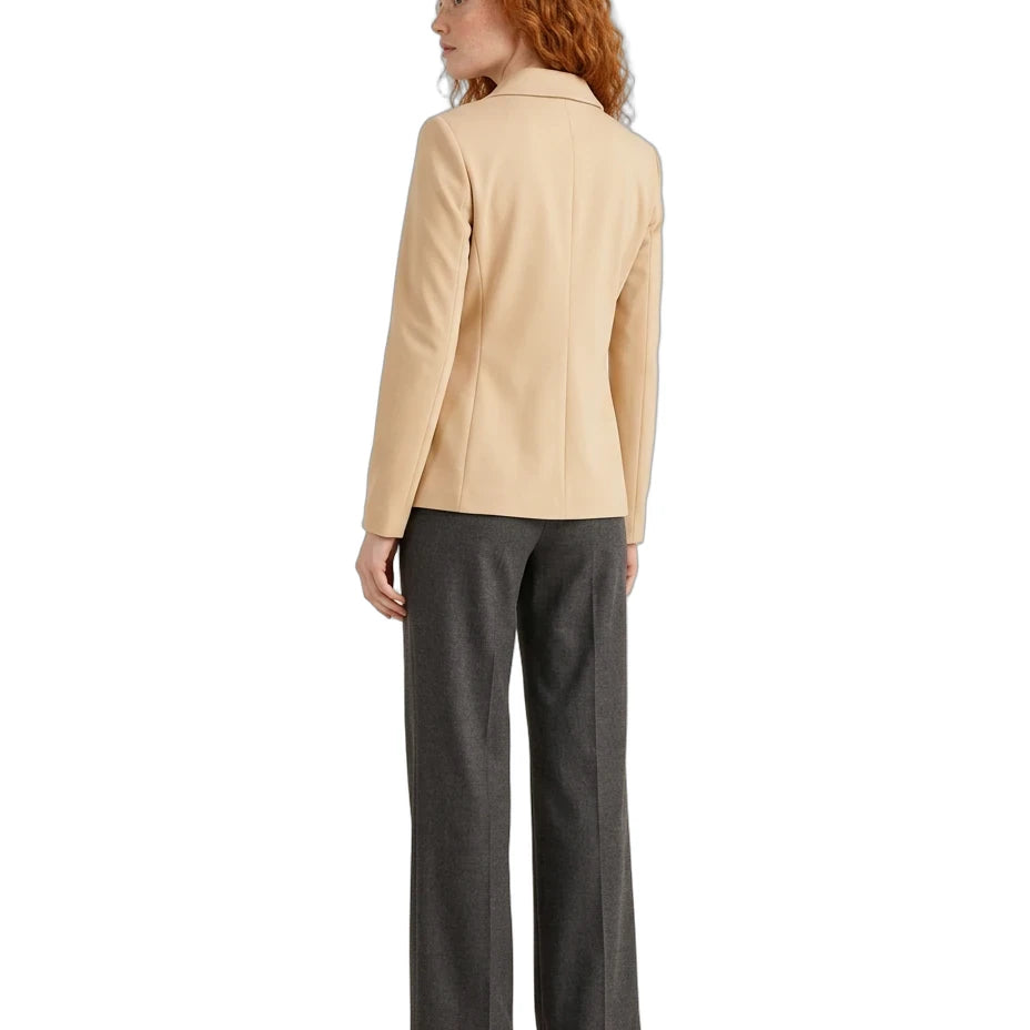 A woman with curly red hair is shown from the back wearing a light beige blazer and dark gray wide-leg trousers, photographed against a solid white background.