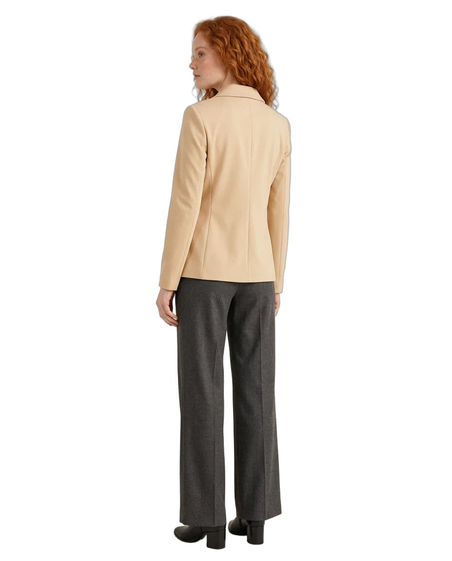 A woman with curly red hair is shown from the back wearing a light beige blazer and dark gray wide-leg trousers, photographed against a solid white background.