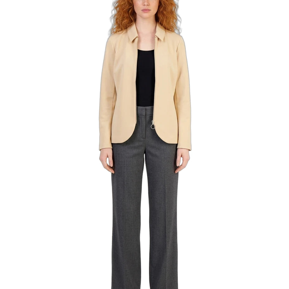 A model with curly red hair stands against a white background wearing a light beige blazer over a black top, paired with dark gray wide-leg trousers and beige flat sandals.
