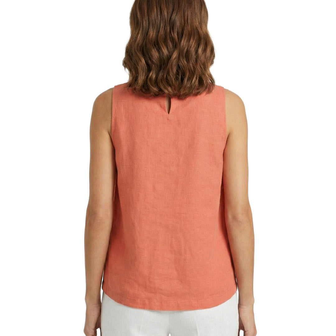 Woman wearing a coral sleeveless top and white pants on a white background