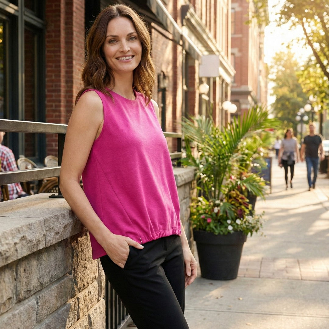 Woman in a pink top standing on a city street with buildings and plants in the background