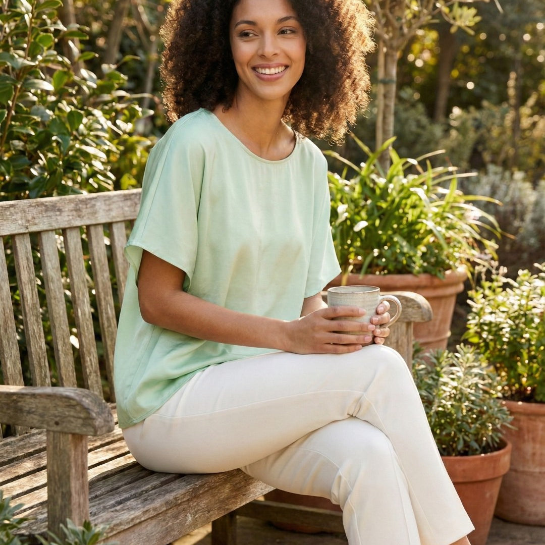 Woman sitting on a wooden bench in a garden holding a mug.