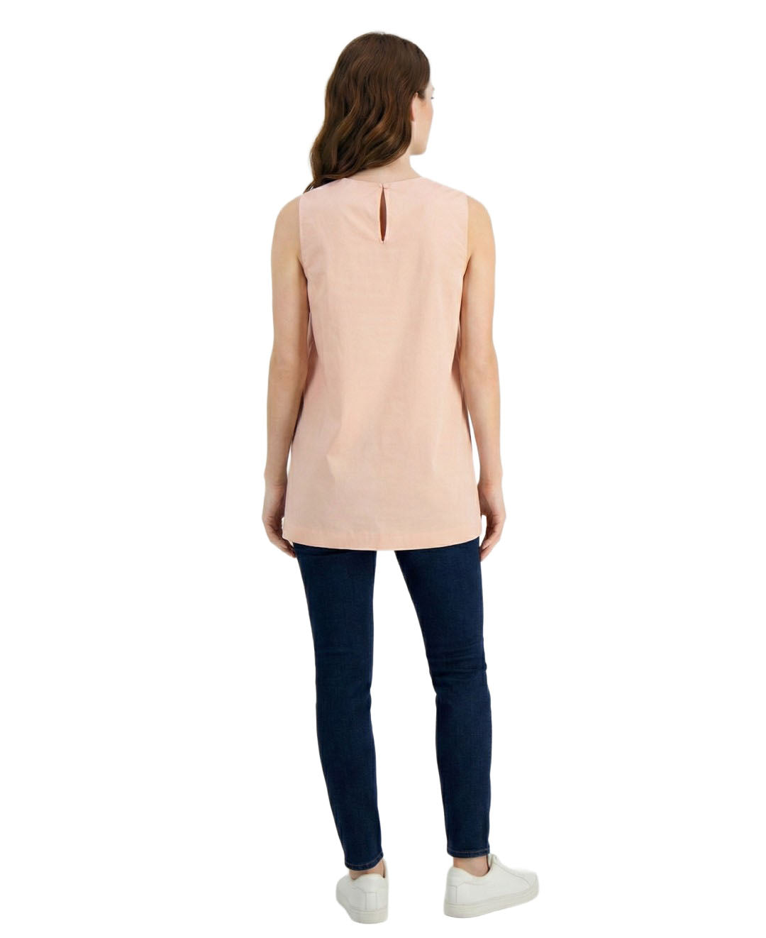 Woman wearing a sleeveless beige top and dark blue jeans on a white background