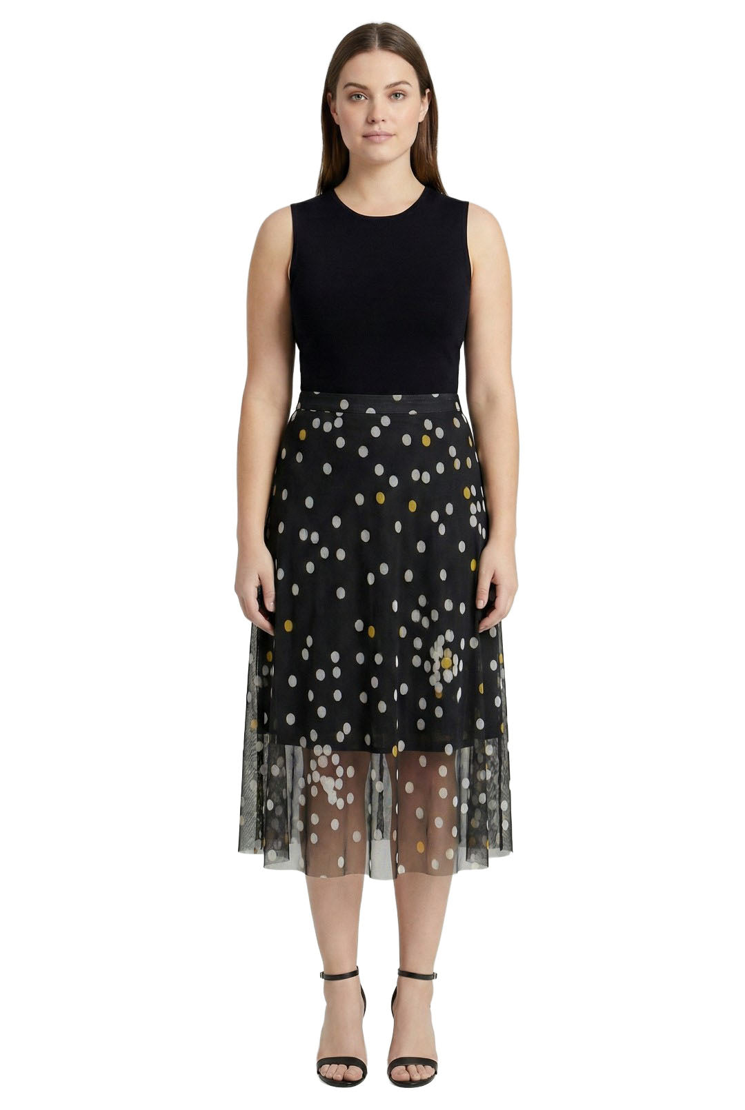 Woman wearing a black sleeveless top and a sheer black skirt with gold polka dots on a white background