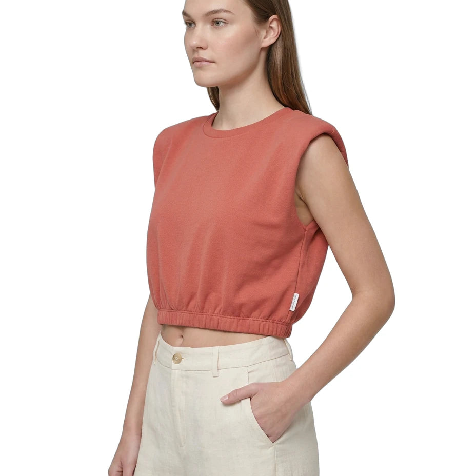 Woman wearing a sleeveless pink top and beige pants on a white background